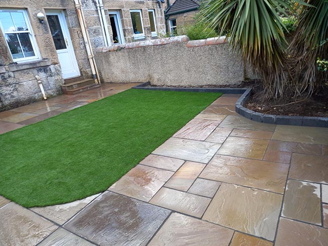 Indian sandstone, multi autumn variation of sizes. Tobermore edging block kerb, stairs capped with Indian sandstone paving, and artificial grass.