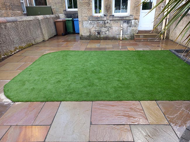 Indian sandstone, multi autumn variation of sizes. Tobermore edging block kerb, stairs capped with Indian sandstone paving, and artificial grass.