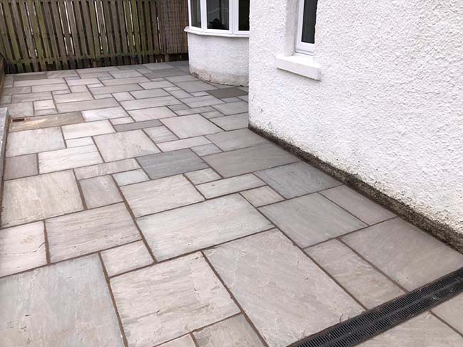 Grey multi sandstone paving with charcoal grey edging kerb.