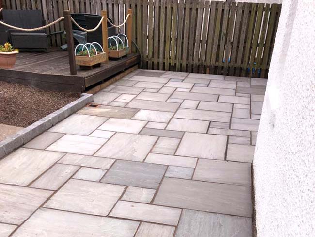Grey multi sandstone paving with charcoal grey edging kerb.